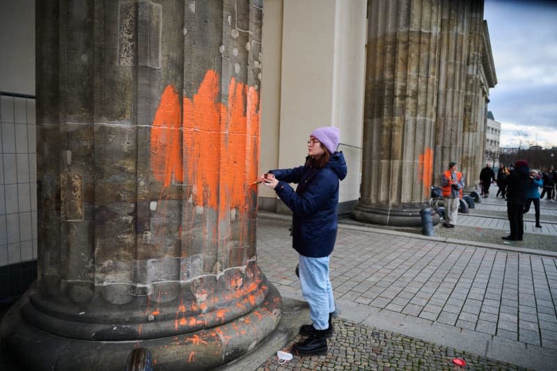 Two climate activists paint the Brandenburg Gate with orange paint. The Last Generation group announced on Thursday that members had painted the west side of the building with paintbrushes. Annette Riedl/dpa