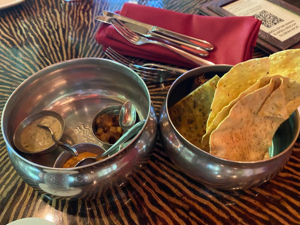 Pieces of bread and three dips in a metal bowl next to the bread