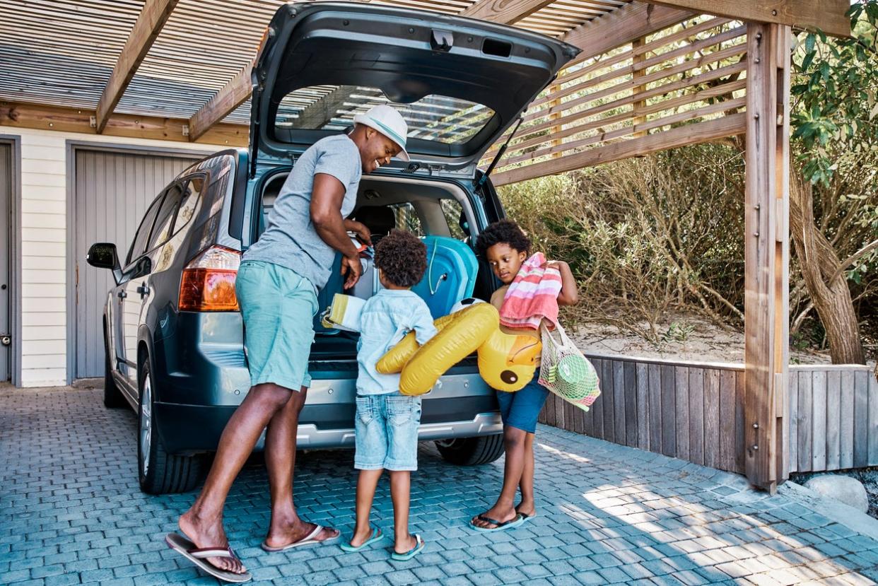 happy father and young sons loading up trunk of open van preparing to go on vacation