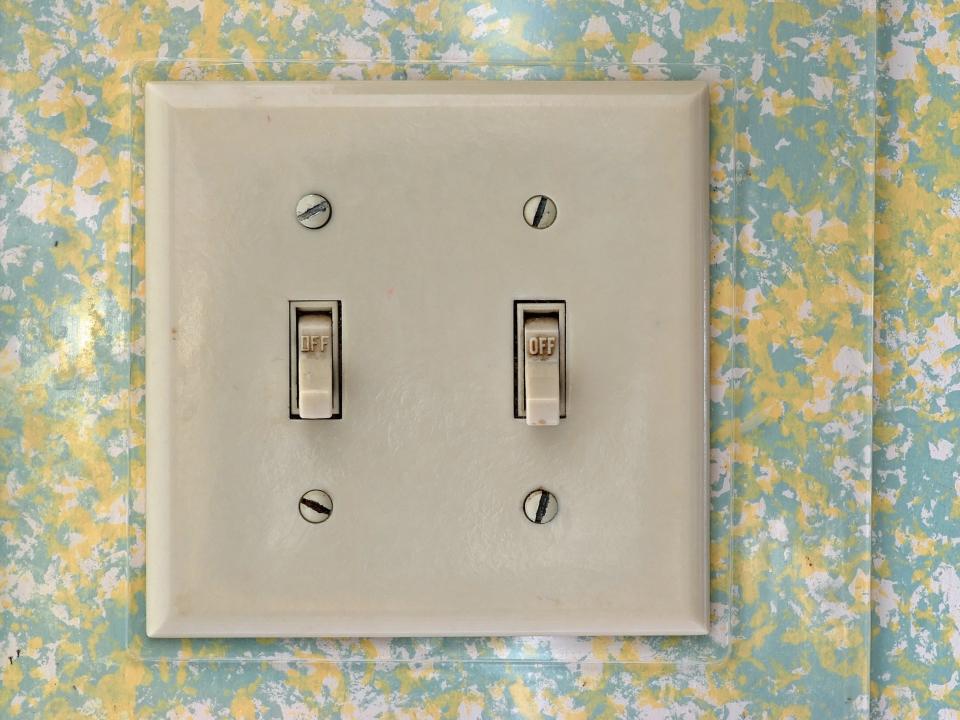 Stained and yellowed plastic light switch and cover with a yellow, white, and blue wall