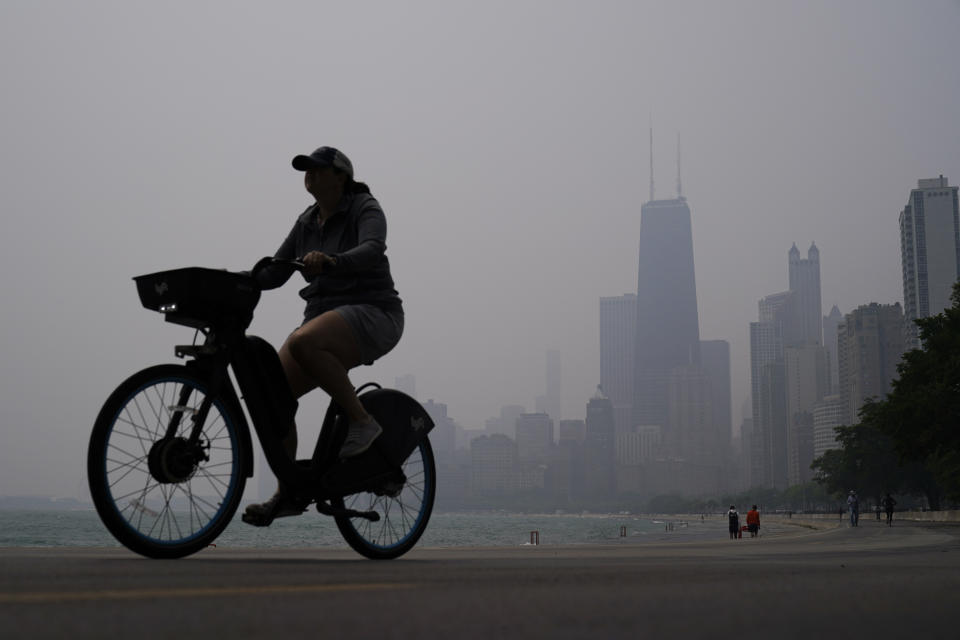 A bicyclist passes along the shore, with high-rises dimly visible across the lake.