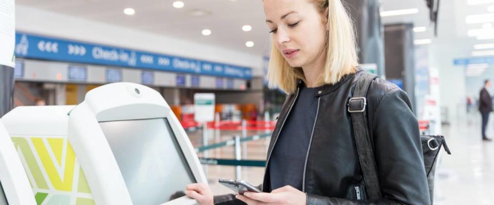 Casual caucasian woman using smart phone application and check-in machine at the airport getting the boarding pass. Modern technology on airport.