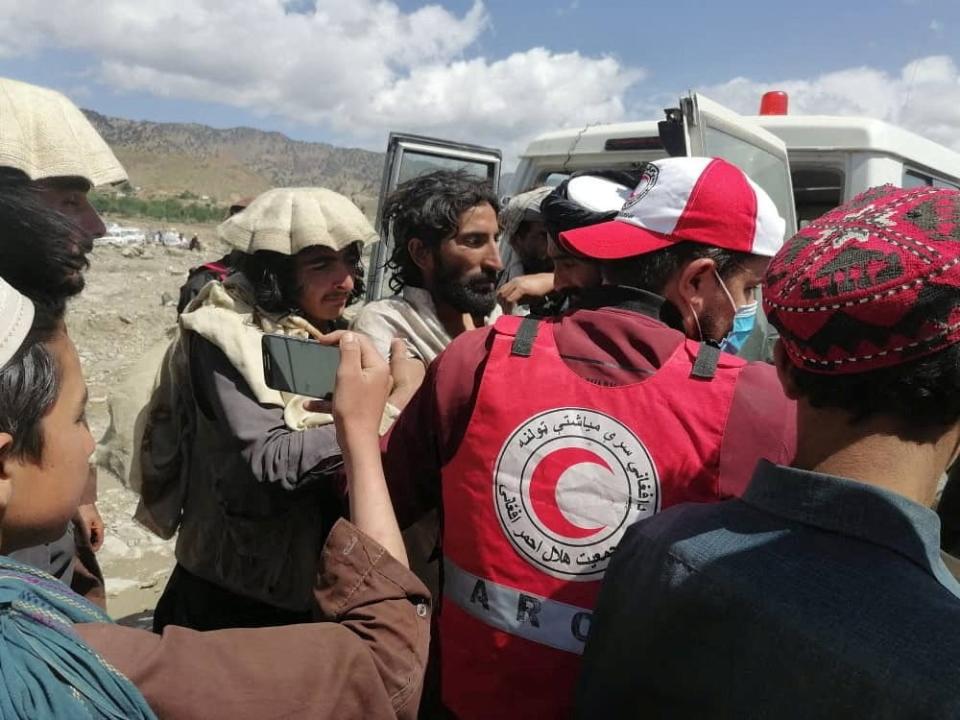 people crowd around a van recording on a phone with medic in red crescent vest