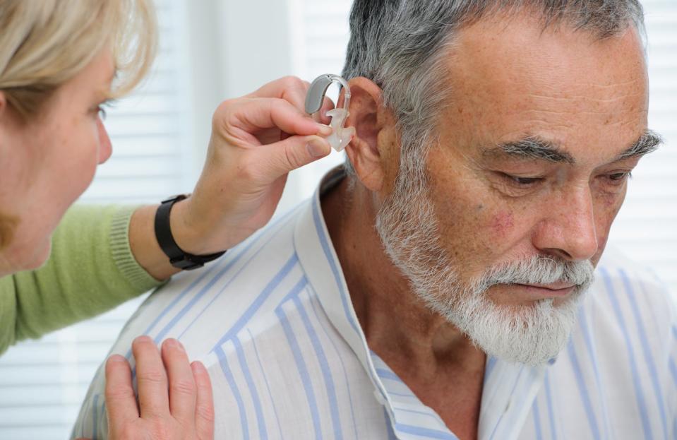 A female doctor inserts a hearing aid inside an older man's ear.