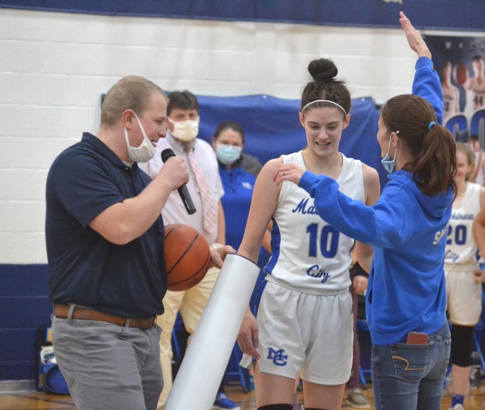Mackinaw City junior center Madison Smith (10) receives a 1,000-point poster from Mackinaw City athletic director Elijah May, while also receiving a hug from her mother, Abbey, during a presentation at half court on Thursday.