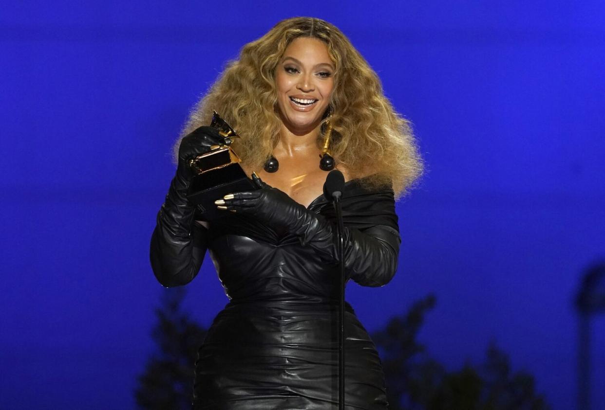 A woman in a black leather dress accepts an award onstage.