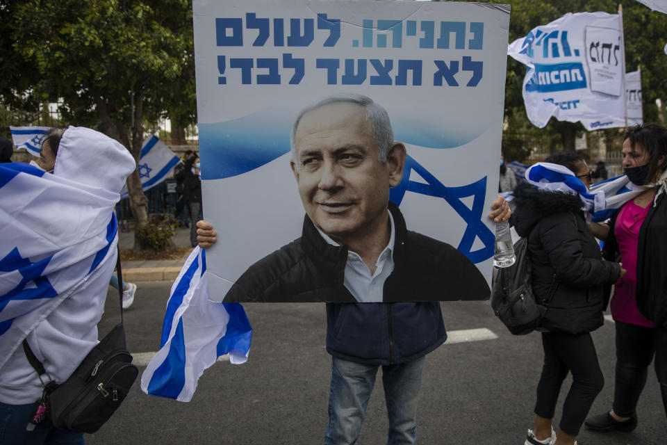 Supporters of Israel's Prime Minister Benjamin Netanyahu hold banners and wave Israeli flags outside his residence in Jerusalem, Sunday, May 24, 2020. Israeli Prime Minister Benjamin Netanyahu was heading to court to face corruption charges in the first criminal trial ever against a sitting Israeli leader. The Hebrew writing say " Netanyahu. you will never walk alone". (AP Photo/Ariel Schalit)