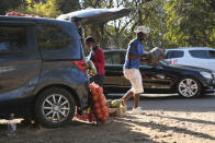 A man carries a bag of potatoes to a customer while selling them from his car by the side of a busy road in Harare, Zimbabwe, Tuesday, June, 23, 2020. Cars have become mobile markets in Zimbabwe where enterprising residents are selling goods from their vehicles to cope with economic hardships caused by the coronavirus. With their car doors and trunks wide open by the side of busy roads, eager sellers display a colorful array of goods in Harare, the capital. (AP Photo/Tsvangirayi Mukwazhi)