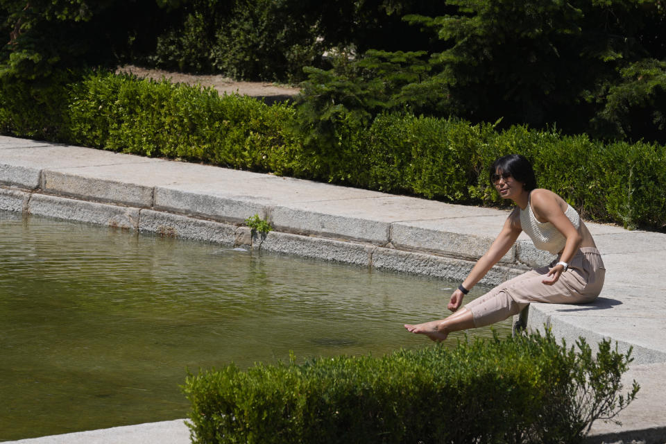 A woman sits by a pond while posing for photos during hot weather in Madrid, Spain, Saturday, July 16, 2022. Temperatures are predicted to rise to around 40 degrees Celsius (104 degrees Fahrenheit) in Madrid with hotter temperatures expected in southern Spain. (AP Photo/Paul White)