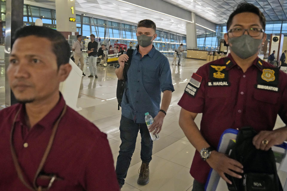 Australian national Bodhi Mani Risby-Jones from Queensland, center, walks with his lawyer Idris Marbawi, left, and an immigration officer upon arrival at Soekarno-Hatta International Airport in Tangerang, Indonesia, Saturday, June 10, 2023. Indonesia’s authorities are deporting an Australian surfer who apologized for attacking several people while drunk and naked in the deeply conservative province of Aceh. Bodhi Mani Risby-Jones was detained in late April on Simeulue Island, a surf resort, after police accused him of going on a drunken rampage that left a fisherman with serious injuries. (AP Photo/Dita Alangkara)