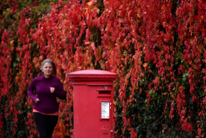 FILE PHOTO: A woman runs past a traditional red Royal Mail post box in London