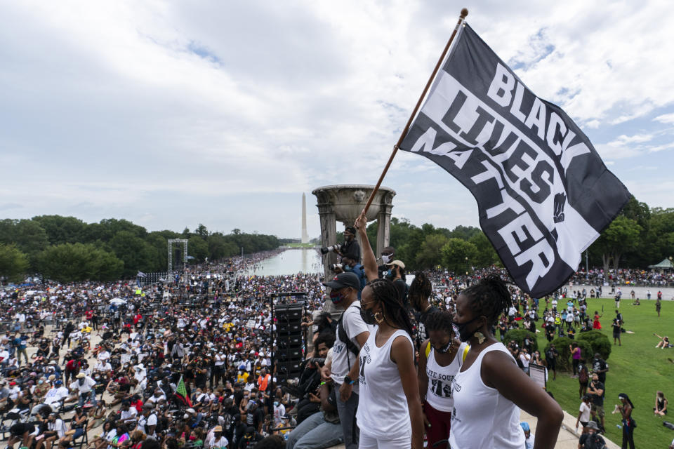 A woman holds a "Black Lives Matter," flag during the March on Washington, Friday Aug. 28, 2020, at the Lincoln Memorial in Washington, on the 57th anniversary of the Rev. Martin Luther King Jr.'s "I Have A Dream" speech. (AP Photo/Alex Brandon)