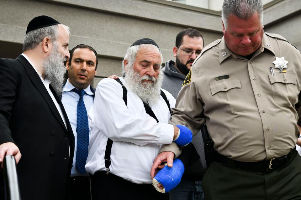 Rabbi Yisroel Goldstein, center, receives assistance from Capt. Jeff Duckworth of the Poway Sheriff's Station, right, following a Sunday afternoon news conference in front of the Chabad of Poway synagogue.