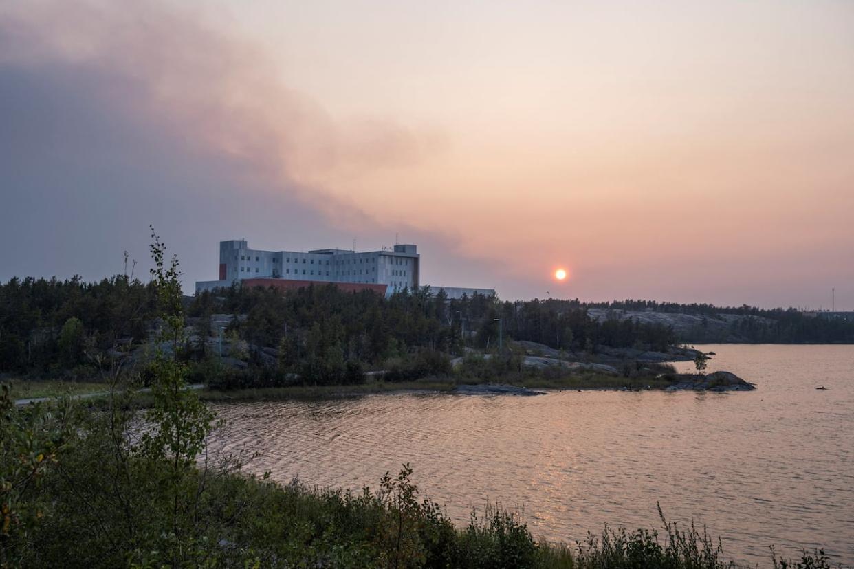 Smoke plumes over Stanton Territorial Hospital, a day after state of emergency was declared due to the proximity of a wildfire in Yellowknife on Aug. 15.  The Northwest Territories Health and Social Services Authority informed evacuees on Friday that they can expect some services to be available again next week. (Pat Kane/Reuters - image credit)