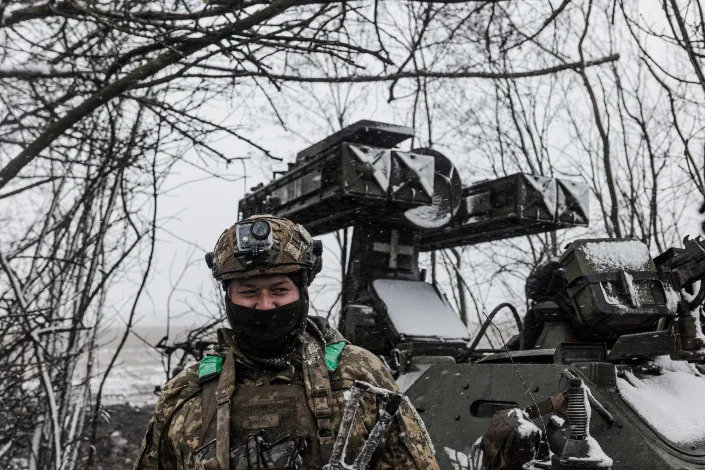 A Ukrainian soldier standing under a tree in front of an anti-aircraft battery in Bakhmut.