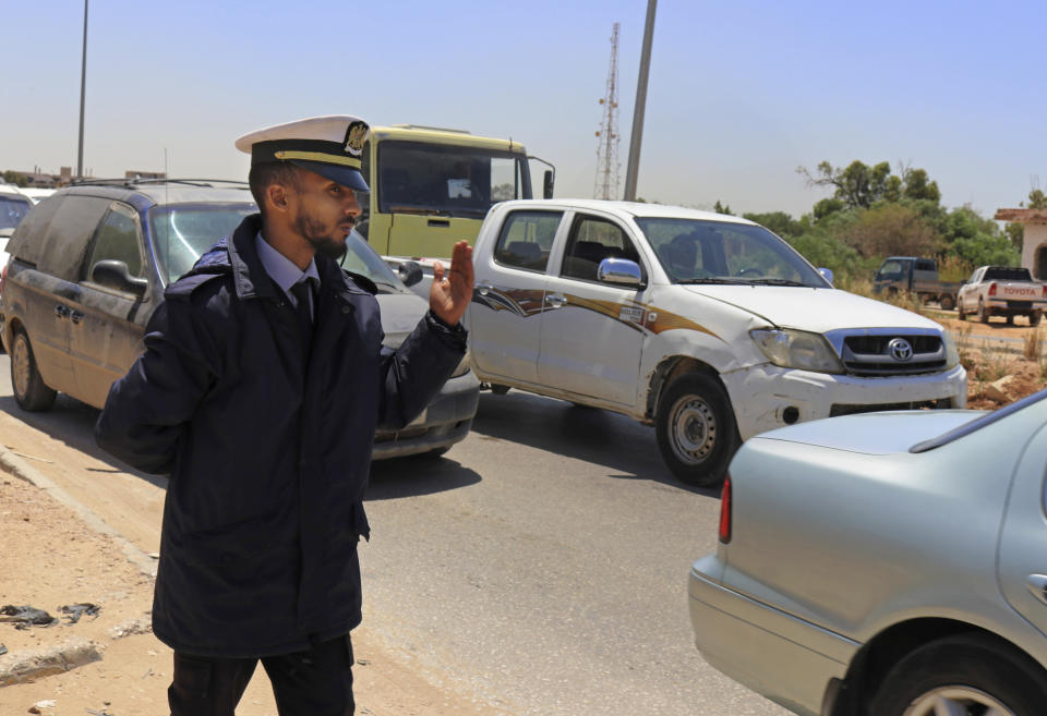 In this May 2, 2019 photo, a police officer waves vehicles through a checkpoint during rush hour in Benghazi, Libya. After years of assassinations, bombings and militia firefights, Libya’s eastern city of Benghazi finally feels safe again -- but security has come at a staggering cost. The city center lies in ruins, thousands of people remain displaced, and forces loyal to Khalifa Hifter, who now controls eastern Libya, have cracked down on dissent. (AP Photo/Rami Musa)