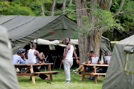 Refugees stand outside one of the tents set up to house the influx of asylum seekers by the Canadian Armed Forces near the border in Lacolle, Quebec, Canada August 10, 2017. REUTERS/Christinne Muschi