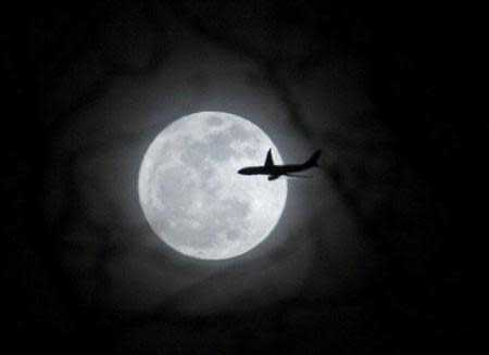 A plane passes in front of a full moon over New York City February 17, 2011. REUTERS/Eric Thayer