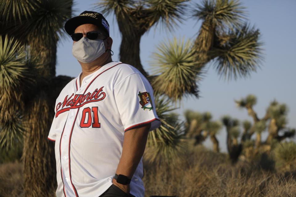 A man in a baseball jersey stands near Joshua trees