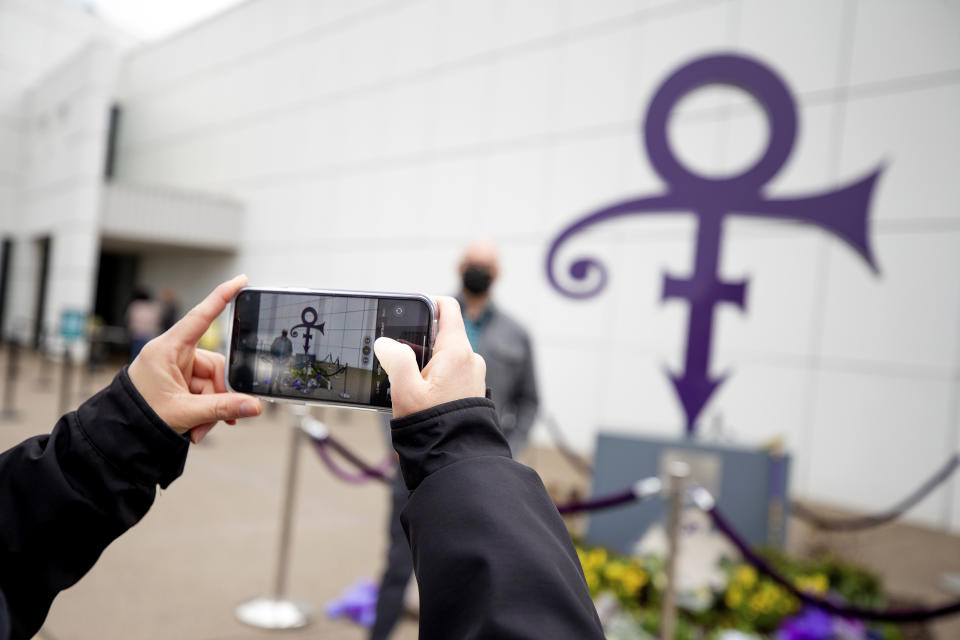 A fan takes a photo of a memorial, Wednesday, April 21, 2021, as others line up to go into Paisley Park in Chanhassen, Minn., on the fifth anniversary of Prince's death. Fans were allowed into the home and studio of the late musician 20 at a time to pay respect. (AP Photo/Stacy Bengs)