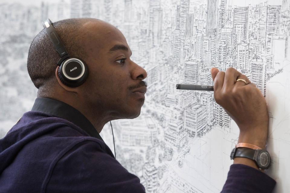 A black man with headphones on draws on a white canvas