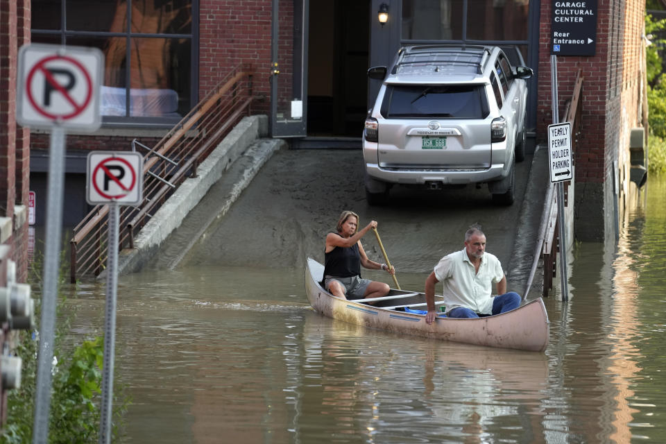 FILE - Jodi Kelly, left, practice manager at Stonecliff Veterinary Surgical Center, behind, and her husband, veterinarian Dan Kelly, use a canoe to remove surgical supplies from the flood-damaged center, July 11, 2023, in Montpelier, Vt. Two of the Vermont communities hardest hit by flooding have put in an urgent request for $3.5 million in state funding to elevate 20 homes in Barre and the capital city of Montpelier for flood victims who still need safe places to live as the state grapples with a housing crisis. They said at a Statehouse press conference on Tuesday, March 19, 2024 that many many whose homes were damaged or lost are still in a state of recovery and saving houses is far cheaper than building new ones. (AP Photo/Steven Senne, file)