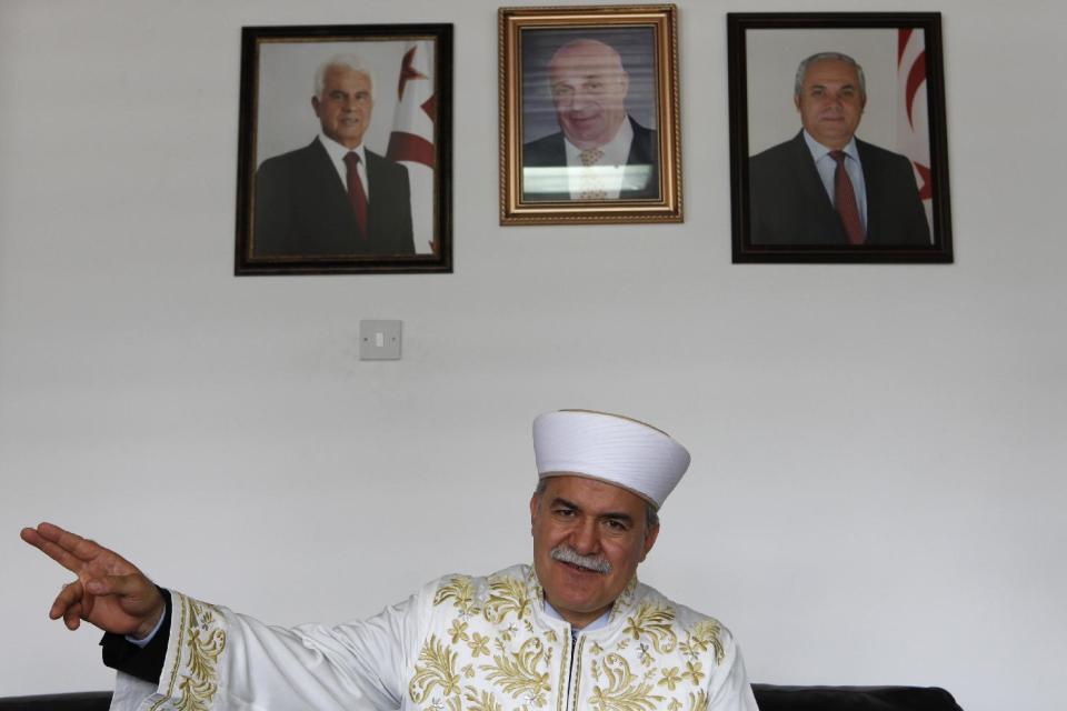 In this photo taken on Monday, April 14, 2014, Cyprus’ Grand Mufti Talip Atalay, the religious affairs leader of Turkish Cypriots in the breakaway north of the ethnically split country, is seen during an interview at his office in northern part of the divided capital Nicosia. In the background are the portraits of the Turkish Cypriot leader Dervis Eroglu, left, and former Turkish Cypriot leader Rauf Denktash, centre. For the first time in nearly 60 years, a Good Friday service was held at the 14th-century church of Agios Georgios Exorinos in the medieval center of Famagusta. Cyprus was divided along ethnic lines in 1974 into a Greek Cypriot south and Turkish Cypriot north after Turkey invaded following a coup aiming to unite the island with Greece. For decades, there was no contact between the religious leaders of the Christian Greek Cypriots and Muslim Turkish Cypriots. But that changed in 2009 with a kind of faith-based diplomacy that has quietly been conducted between the leader of the island’s Greek Orthodox Christian Church Archbishop Chrysostomos II and Turkish Cypriot Muslim Grand Mufti Talip Atalay. (AP Photo/Petros Kardjias)