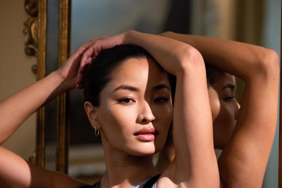 A woman rests her hands on top of her head and a shadow partially covers her face.