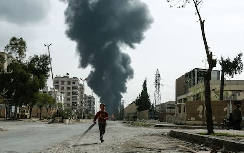 A child runs along a street in front of clouds of smoke billowing following a reported air strike on Douma, the main town of Syria's rebel enclave of Eastern Ghouta - Credit: AFP