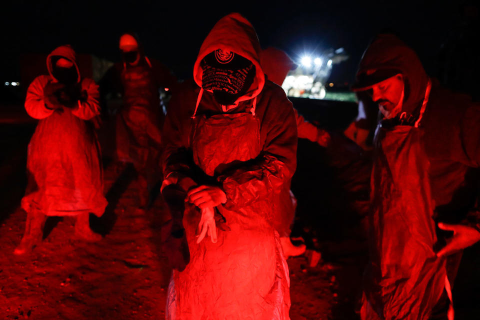 <p>Farmworker Eduardo Garcia, of Mexicali, Mexico, center, puts on an apron and gloves in the glow from the taillights of a bus, as he and his crew arrive at a cabbage field ready for harvest, before dawn outside of Calexico, Calif., March 6, 2018. (Photo: Gregory Bull/AP) </p>