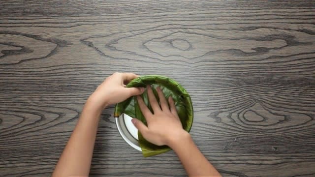 Folding banana leaf down into a round baking tin 