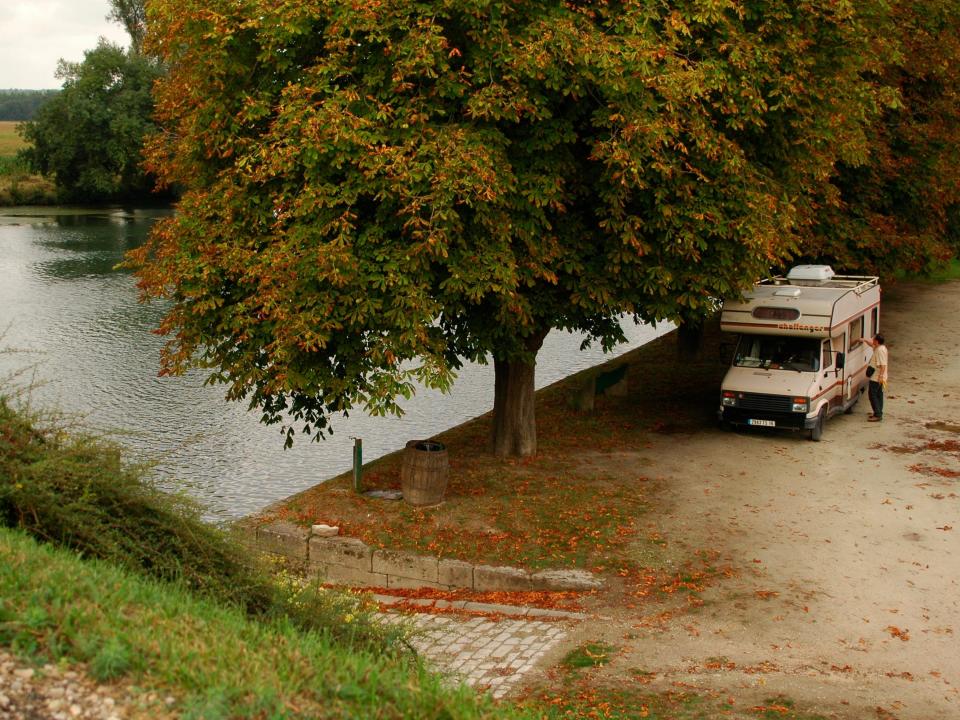 An RV parked by a body of water next to a tree.