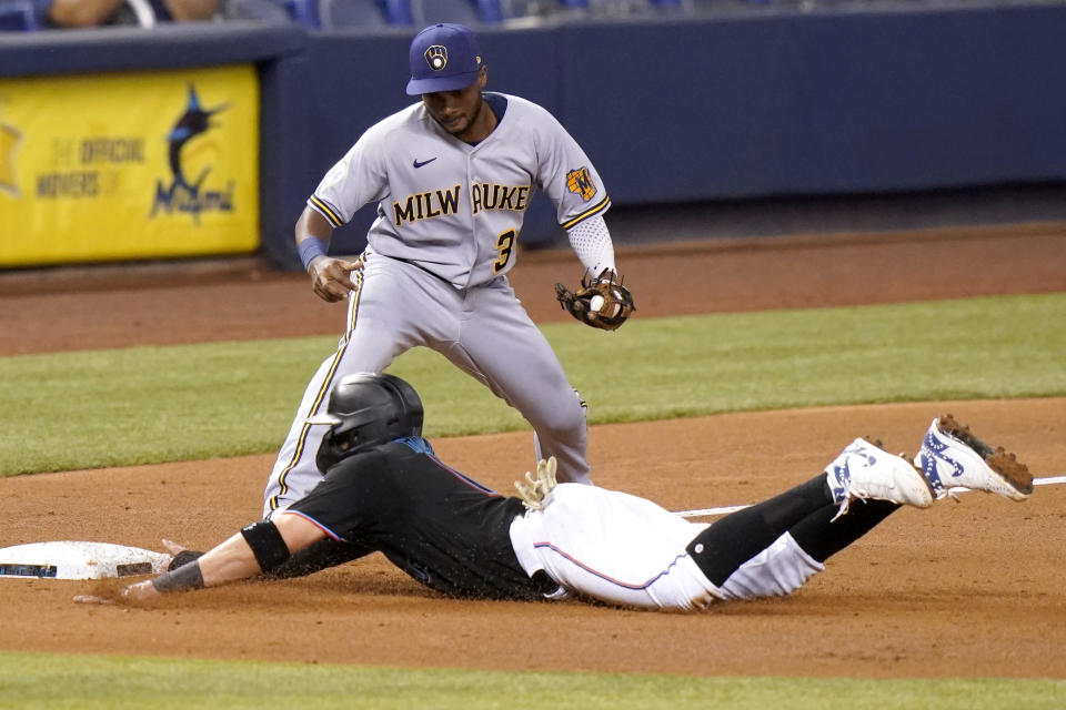 Miami Marlins' Miguel Rojas, bottom, slides past Milwaukee Brewers third baseman Pablo Reyes (33) as he is safe on a single hit by Garrett Cooper during the third inning of a baseball game, Friday, May 7, 2021, in Miami. (AP Photo/Lynne Sladky)