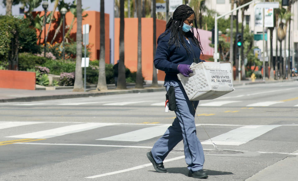 LOS ANGELES, CALIFORNIA  - MARCH 24: A U.S.Postal Service worker wears a face mask and gloves while crossing a downtown street as the coronavirus pandemic continues on March 24, 2020 in Los Angeles, California. California Governor Gavin Newsom issued a ‘stay at home’ order for California’s 40 million residents in order to slow the spread of COVID-19. (Photo by Mario Tama/Getty Images)