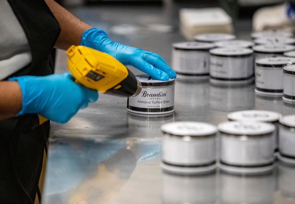 A worker hand shrink wraps packages of almond toffee bites at Brandini Toffee in Rancho Mirage, Calif., Thursday, Oct. 26, 2023.