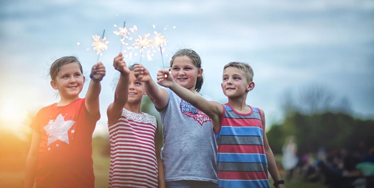 four friends holding lit sparklers in air, a time honored 4th of july activity