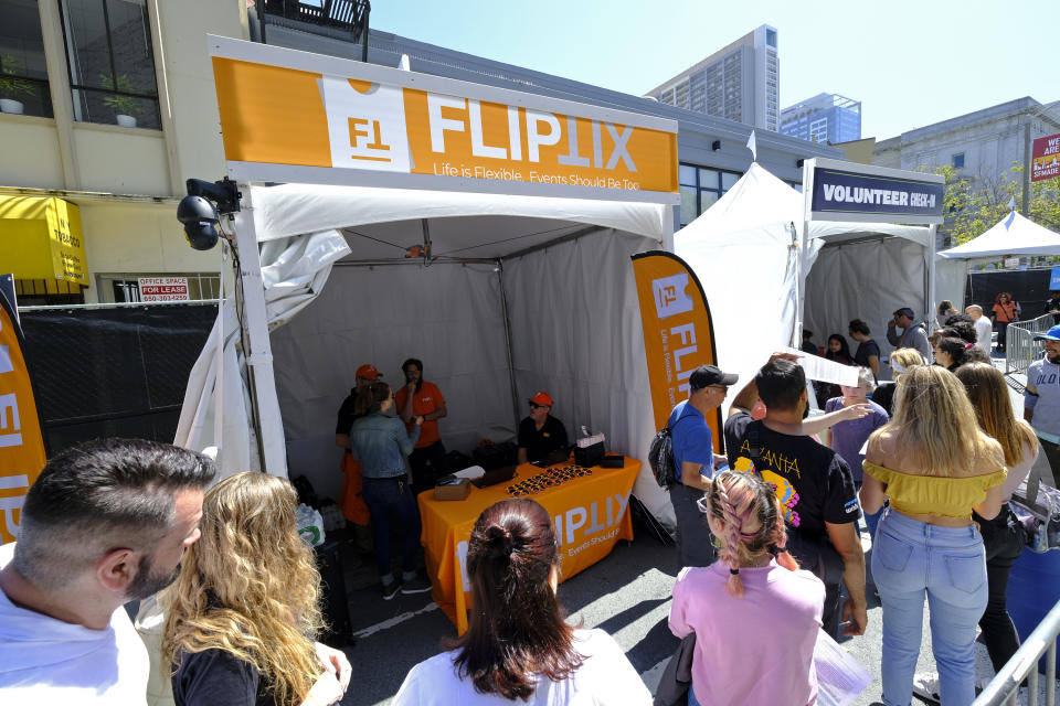 In this photo taken Friday, June 21, 2019, FlipTix CEO Jaime Siegel, seated, works at his company's tent at the entrance to the Clusterfest comedy event in San Francisco. The company's application lets people who leave a venue early sell their ticket and lets someone who wants the remainder of the ticket buy it. Event organizers hoping to eliminate ticket scams and huge markups in the secondary market are increasingly turning to companies that use technology to allow fans to buy and resell their tickets while putting caps on prices.(AP Photo/Eric Risberg)