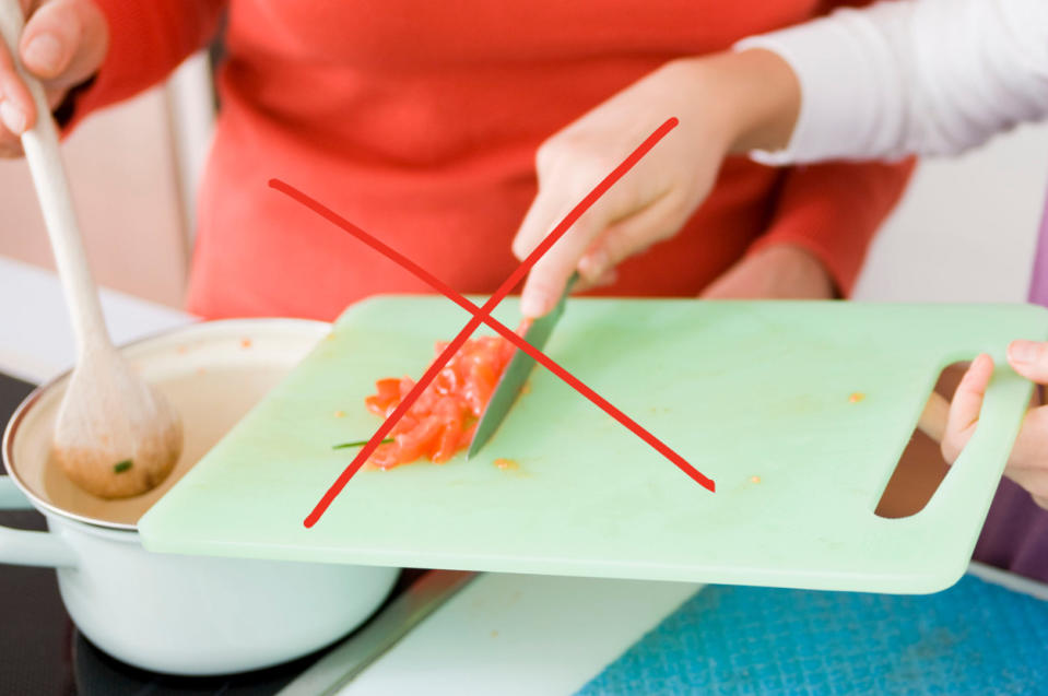 A person incorrectly using the blade to push food from a cutting board into a sauce pan.