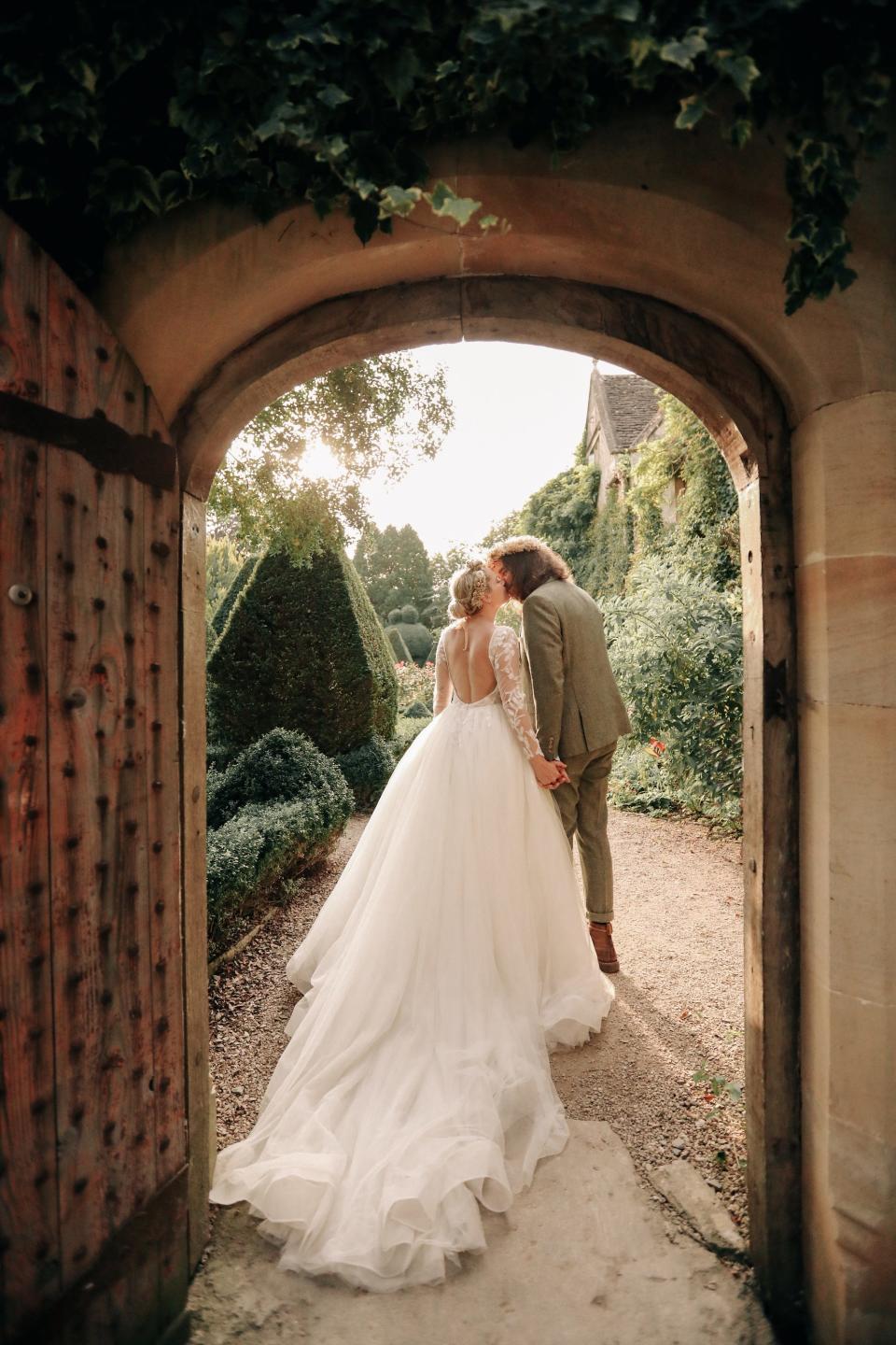 A couple kisses as they walk through a doorway on their wedding day.