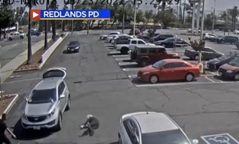 81-year-old carjacking victim is seen in grab from surveillance video on ground in lower left as thief pulls her SUV, with its rear hatch door open, out of the spot it was in on May 24, 2022. / Credit: Redlands, Calif. police