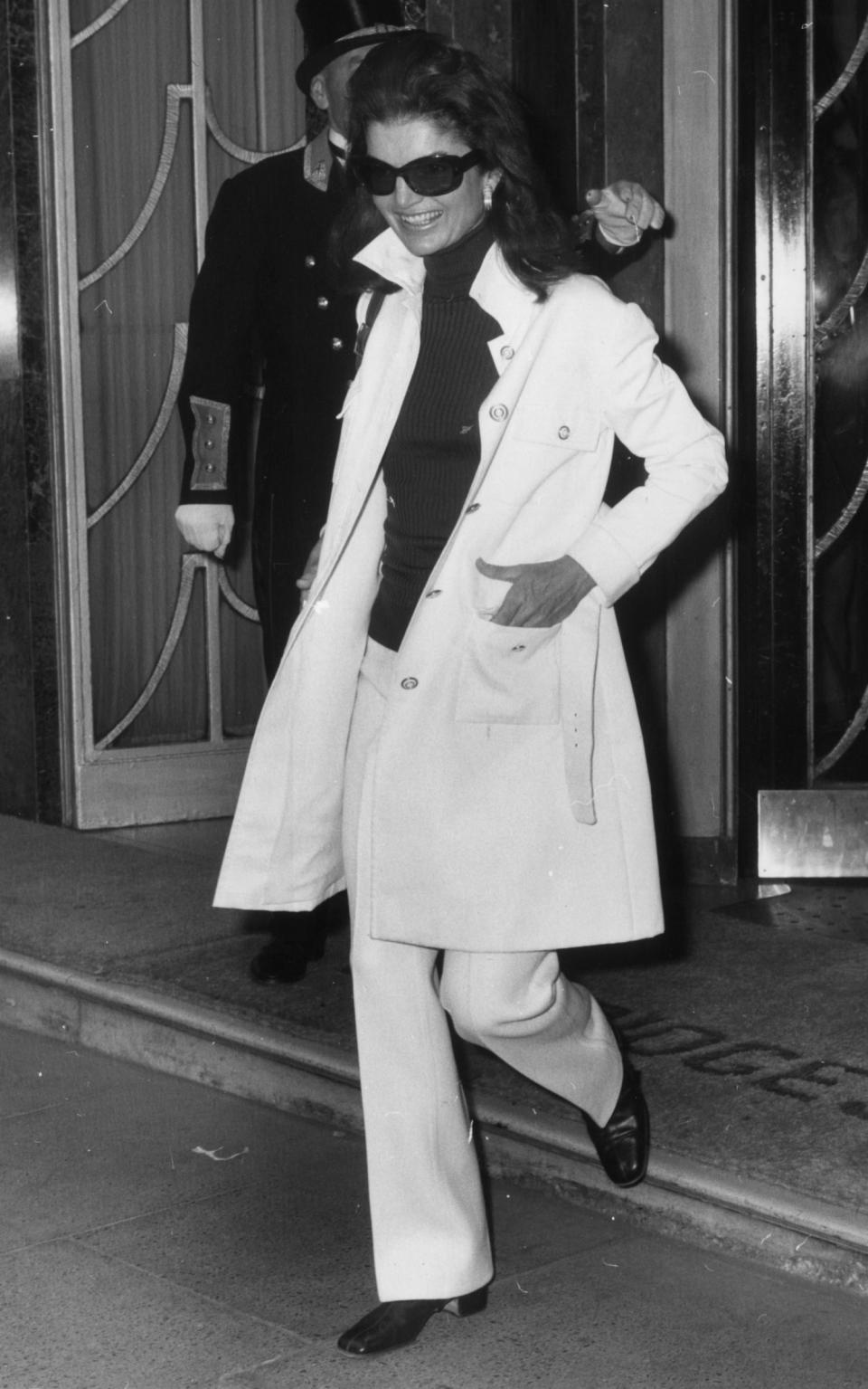 Jackie Onassis wearing a Safari style jacket over flared hipster trousers and a polo neck jumper.