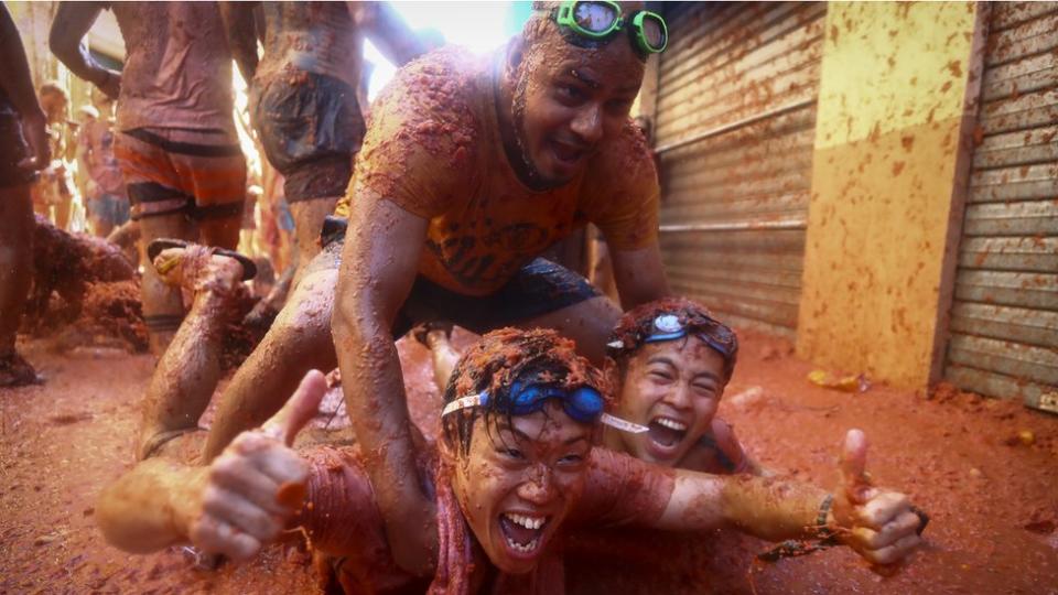 Three men covered in tomatoes lying in a street coated in tomato juice