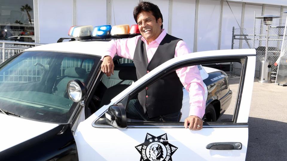 Erik Estrada poses with a police car, 2019