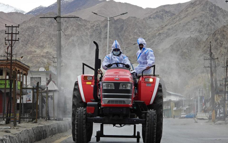 Health workers wearing protective gear ride a tractor as they sanitise a street with disinfectant in Leh - Mohd Arhaan ARCHER / AFP