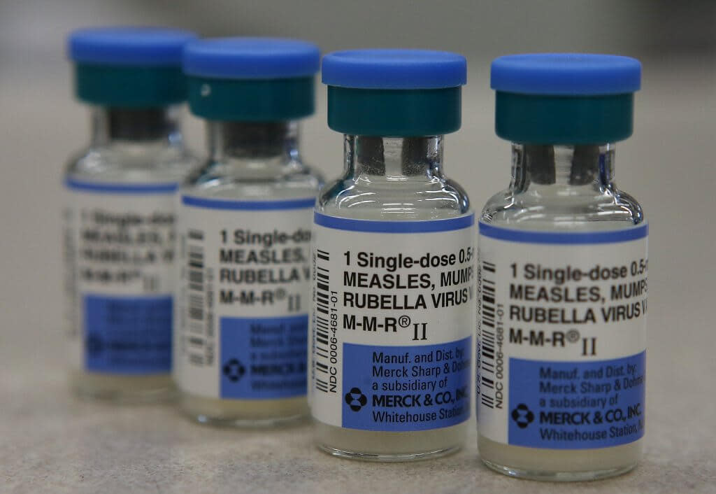 A row of four bottles of 1-single dose measles, mumps and rubella virus vaccine bottles with a white and blue labels and blue lids.