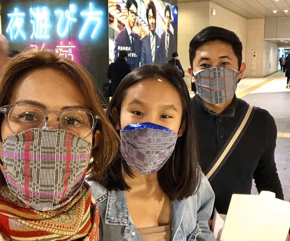 In this late February 2020, photo, Carlo Navarro poses behind wife Evie and daughter Gia for a family photo while wearing face masks during a trip to Tokyo. Days after he was cleared and discharged from hospital, Carlo Navarro shared his COVID-19 experience on a Facebook public post. (Carlo Navarro via AP)