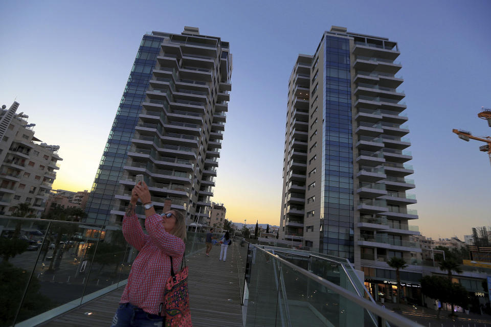 FILE - In this Friday, July 6, 2018 file photo, a woman on the bridge takes a selfie with The Twins buildings in the background, one of a number of new high-rises transforming the skyline view, in the southern coastal city of Limassol in the eastern Mediterranean island of Cyprus. Cyprus government spokesman Kyriakos Koushos said on Tuesday, Oct. 13, 2020, that the Cabinet accepted a recommendation by the minsters of the interior and finance to cancel altogether the "golden passport" program that has netted billions of euros over several years. Koushos said the decision was based on the Cyprus Investment Program's "long-standing weaknesses, but also the abuse" of its provisions. (AP Photo/Petros Karadjias, File)