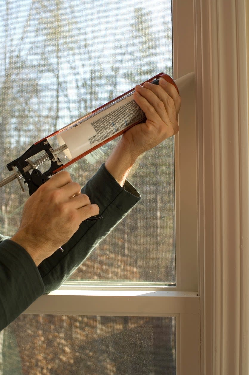 person using a caulking gun to caulk windows