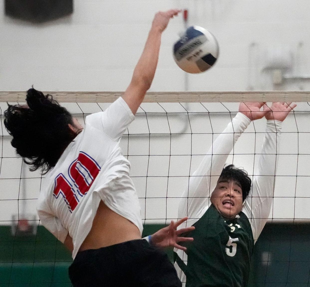 Cranston East Thunderbolt setter, Larry Yin, goes up on the net to block a spike from Mountie Azariah Chauvin last year.
