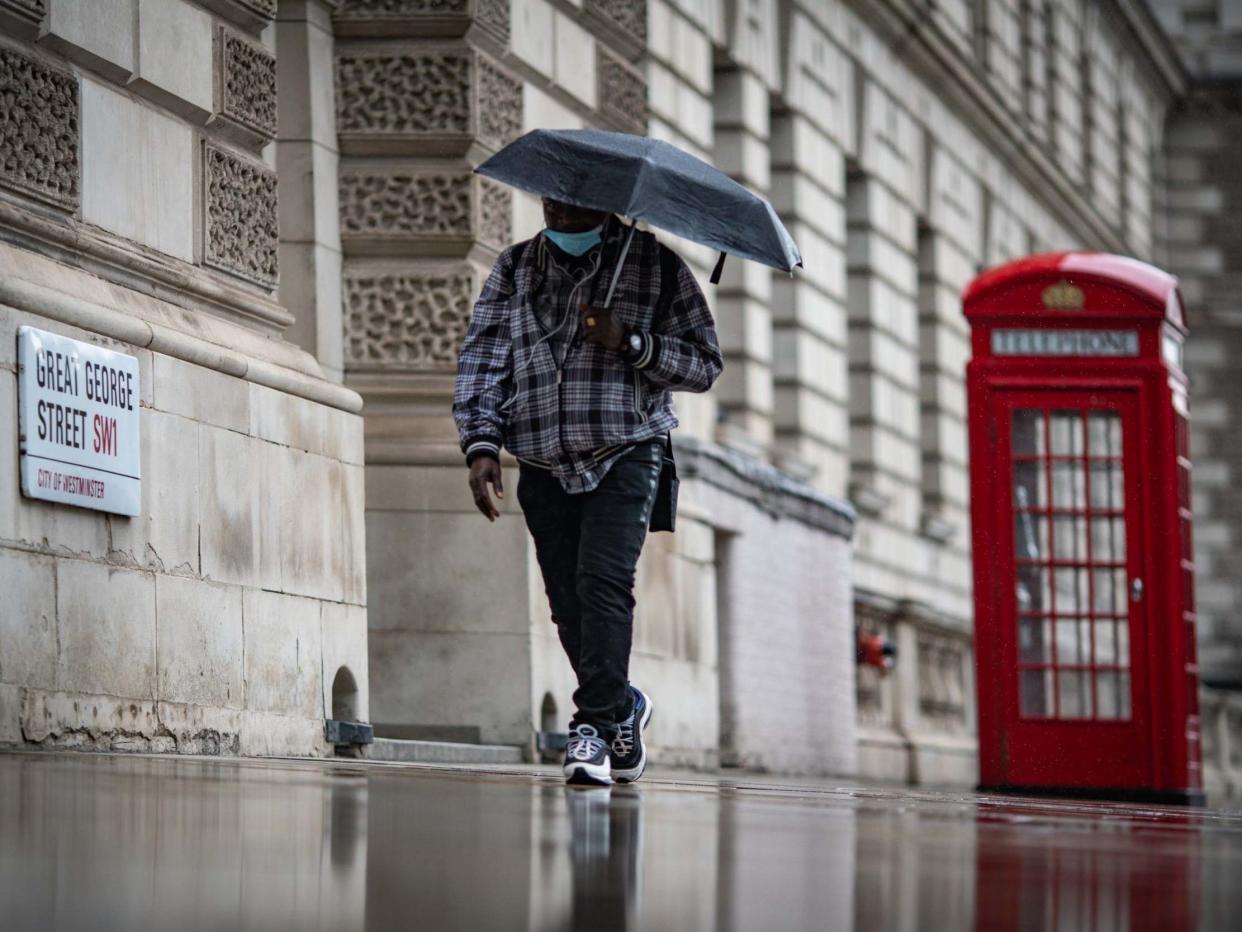 A man shelters from the rain under an umbrella in Westminster: PA